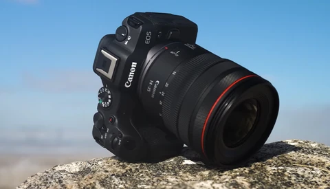 Canon EOS DSLR camera with telephoto lens positioned on a rocky surface against a clear blue sky.
