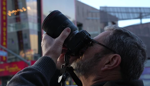 Photographer holding binoculars to his eyes while looking toward an urban skyline during golden hour.