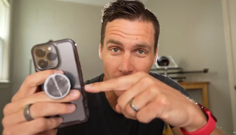 Man holding a smartphone with a magnetic ring attachment, pointing at the device's camera system.