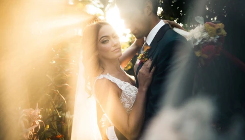 Bride and groom embrace outdoors with dramatic golden sunlight and smoke effects surrounding them.