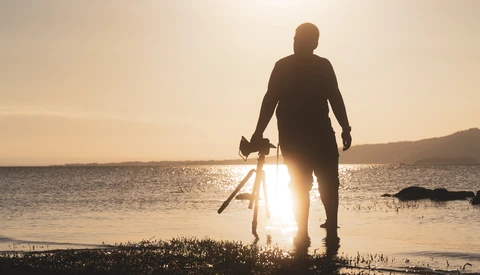Silhouetted surfer carrying surfboard walking into ocean at golden hour.