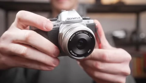 Hands holding an Olympus mirrorless camera with a prime lens attached.