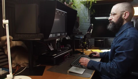 Photographer working at a desk with dual monitors in a dark studio space.