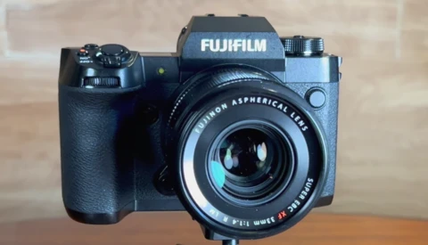 Fujifilm mirrorless camera with Fujinon aspherical lens mounted, displayed against a neutral background.