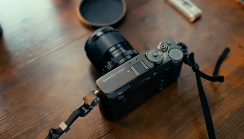 Mirrorless camera with attached lens and shoulder strap on wooden surface.