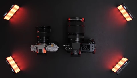 Two mirrorless cameras with lenses surrounded by four red and amber LED panel lights on dark background.