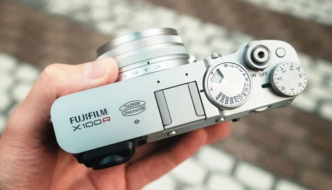 White Fujifilm X100R rangefinder camera held in a hand, showing its manual controls and silver lens.