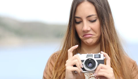 Woman holding a vintage rangefinder camera while looking down at the viewfinder outdoors.