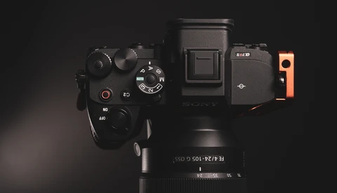 Overhead view of a mirrorless camera with electronic viewfinder, grip extension, and telephoto lens on black surface.