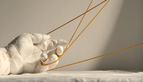 White-gloved hand holding golden strings against a neutral background with dramatic side lighting.
