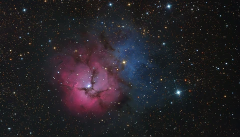 Deep space nebula with pink emission clouds and blue reflection nebula surrounded by stars.