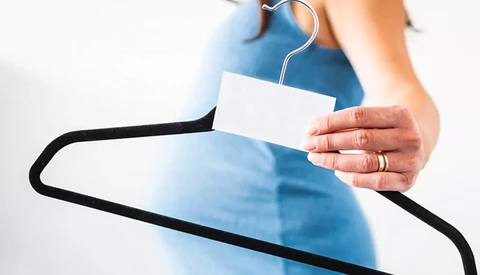 Person holding a clothing hanger with a blank white price tag or label attached.