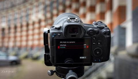 Mirrorless camera mounted on tripod displaying menu settings with urban brick building backdrop.