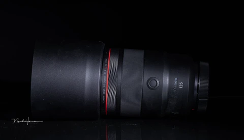 Canon RF 135mm telephoto lens positioned horizontally against black background with red accent band visible.