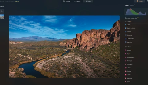 Aerial view of a winding river through desert landscape with rocky hills and sparse vegetation.