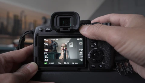 Photographer holding a mirrorless camera with electronic viewfinder extended, displaying live view on rear LCD screen.