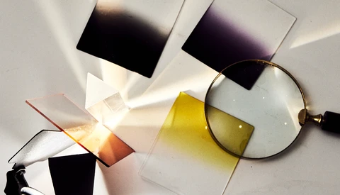 Color filter swatches and a magnifying glass arranged on white paper with warm sunlight casting shadows.