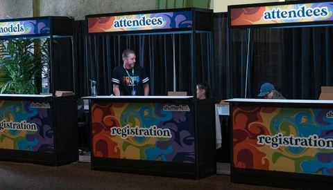 Three registration booths with colorful geometric designs and attendee staffing at what appears to be an event or conference venue.