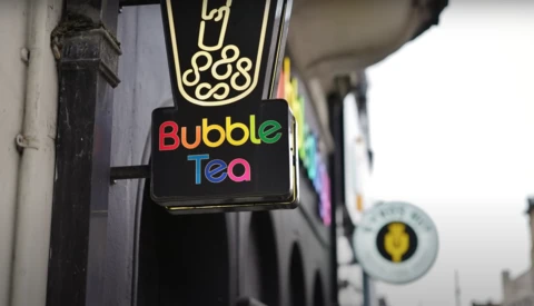 Neon sign for a bubble tea shop with illuminated logo and colorful lettering against storefront.