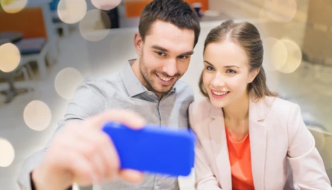 Two smiling business professionals taking a selfie with a blue smartphone.