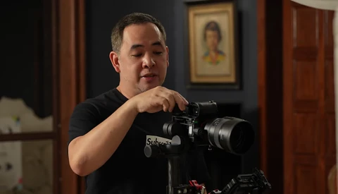 Videographer operating a cinema camera mounted on a tripod in an interior setting.
