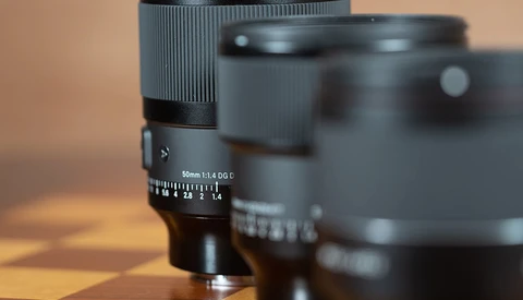 Close-up of a 50mm f/1.4 lens with focus ring and aperture scale visible, with additional lenses blurred in the background.