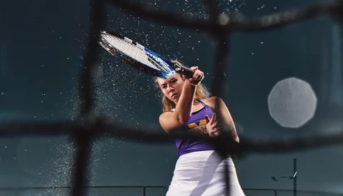 Tennis player mid-swing with water droplets frozen in motion around her racket.