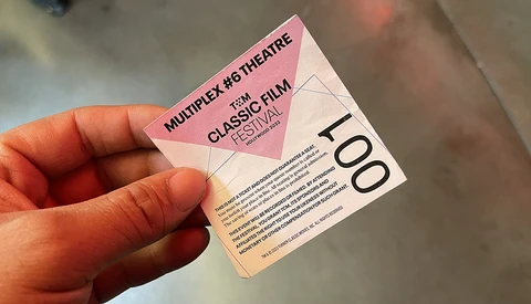 Hand holding a pink multiplex theater ticket stub for a classic film festival.
