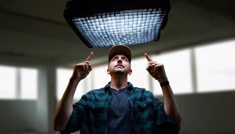 Man in plaid shirt and cap gazes upward at a large grid-pattern ceiling light fixture.