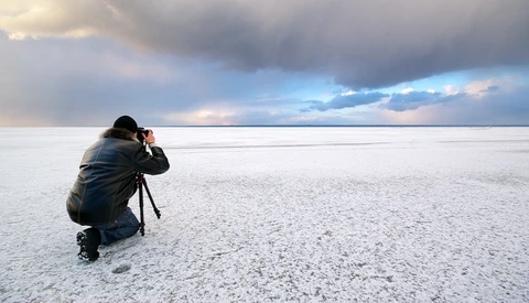 Photographer crouching on a salt flat to capture the dramatic sky reflected in the water.