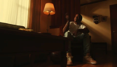 Person sitting on floor in warm interior lighting, gazing toward window light source.