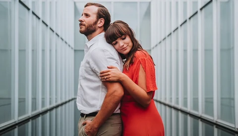 Couple posing together in a modern corridor with symmetrical glass and metal walls.