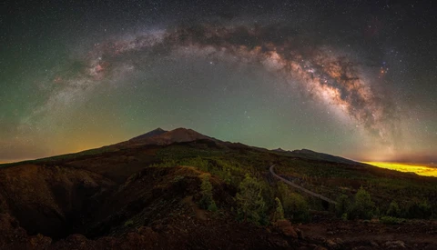 Milky Way arcing over a volcanic mountain silhouette at night.