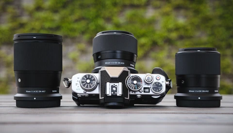 Vintage rangefinder camera with three interchangeable lenses arranged symmetrically on wooden surface.