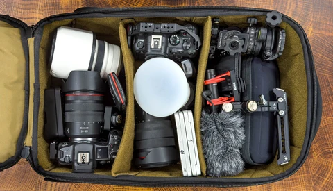 Open camera equipment case with DSLR body, lenses, microphone, audio recorder, and accessories organized in padded compartments.