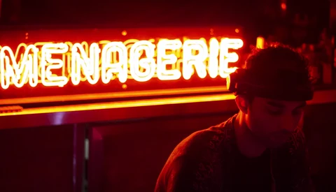 Person silhouetted against a glowing neon sign with warm red and yellow lighting.
