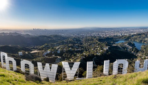 Large white letters spelling "HOLLYWOOD" on a hillside overlooking a sprawling cityscape with mountains in the distance.