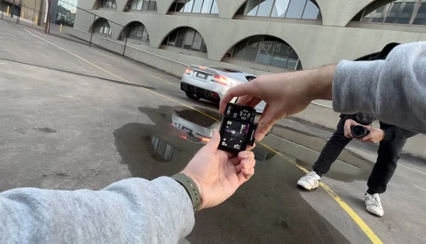 Photographer's hands holding a smartphone displaying camera settings while standing in an urban plaza.