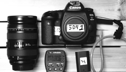 Canon EOS 5D Mark IV camera body with Sigma 24-70mm lens, Profoto flash trigger, and accessories on white wood surface.