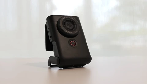 Black compact camera with red power button mounted on white surface against blurred background.