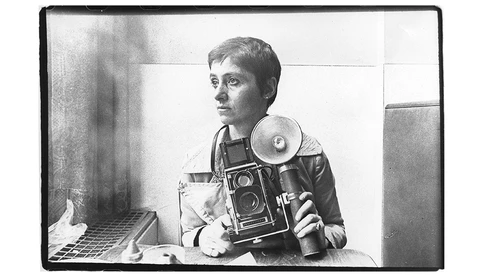 Black and white self-portrait of a photographer holding a large format camera and light meter.