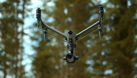 DJI Inspire 3 drone hovering against a blurred forest canopy backdrop.