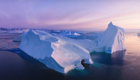 Large icebergs floating in calm ocean water during twilight with purple and pink sky.