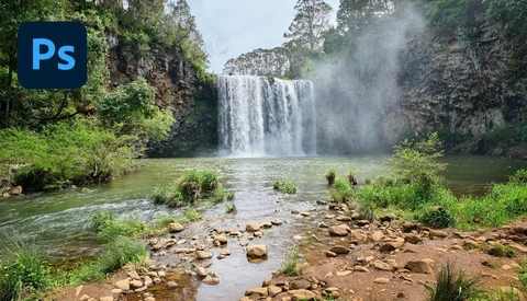 Powerful waterfall cascading into a misty pool surrounded by lush green vegetation and rocky banks.