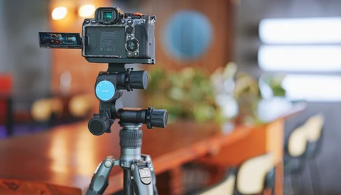 Professional camera mounted on tripod with articulating arm and ring light in studio setting.