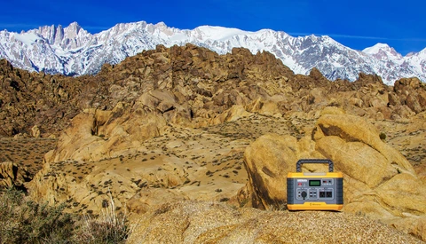 Portable power station on desert rocks with snow-capped mountains in background.