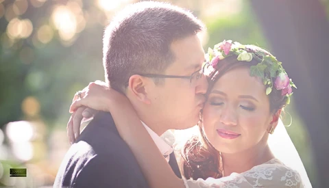 Groom kissing bride's cheek during golden hour, bride wearing flower crown and lace veil.