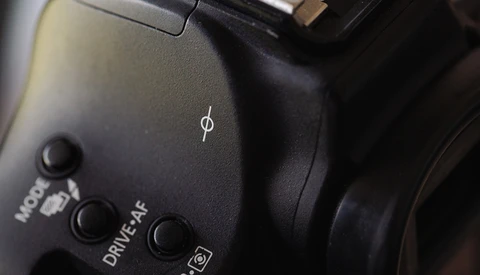 Close-up of camera body controls showing mode dial, drive settings, and ISO button with dramatic side lighting.