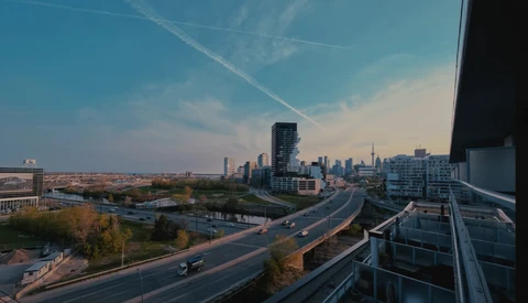 Urban skyline with elevated highway and green park space during golden hour.