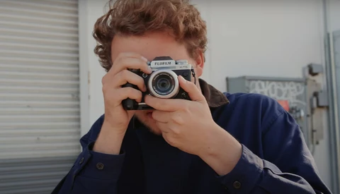 Person holding a Fujifilm rangefinder camera up to their face, preparing to take a photograph.